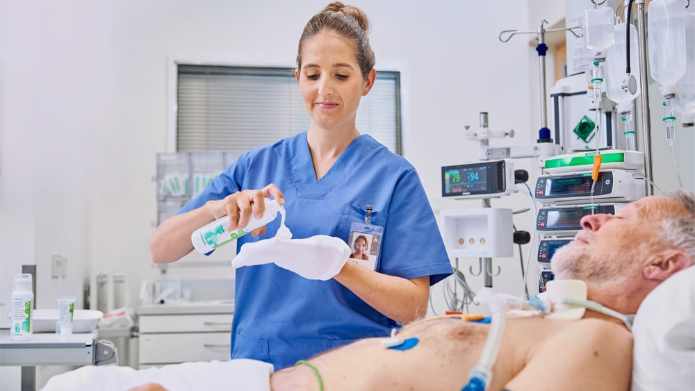 Krankenschwester hält Prontoderm Schaumstoff im Krankenhaus vor einem älteren Patienten, der im Bett liegt und ihn mit einem Handschuh anlegt