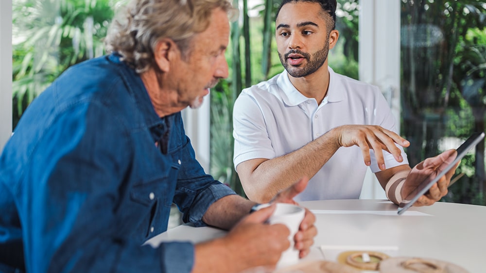 Un vieux homme avec un café et un jeune homme avec une tablette sont assis à une table et parlent