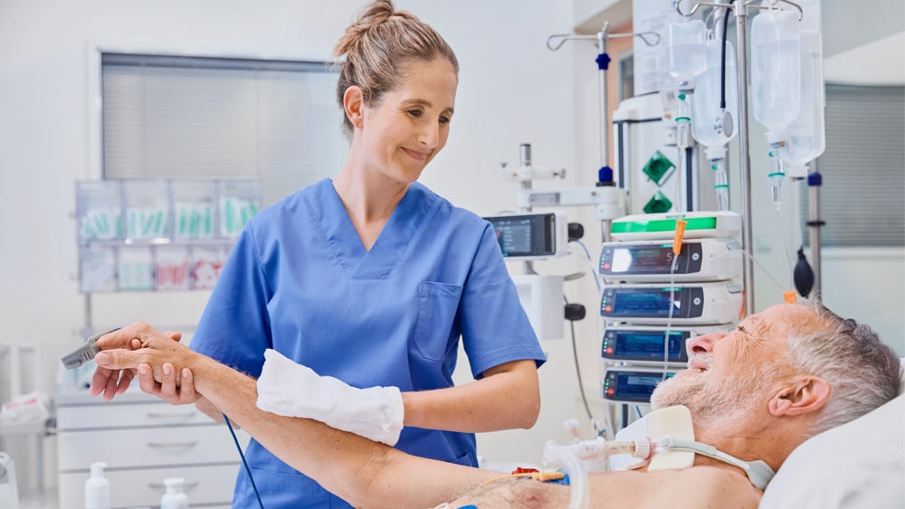 Patient im Krankenhausbett. Die Pflegekraft dekolonisiert den Oberarm des Patienten mit einem Tuch.