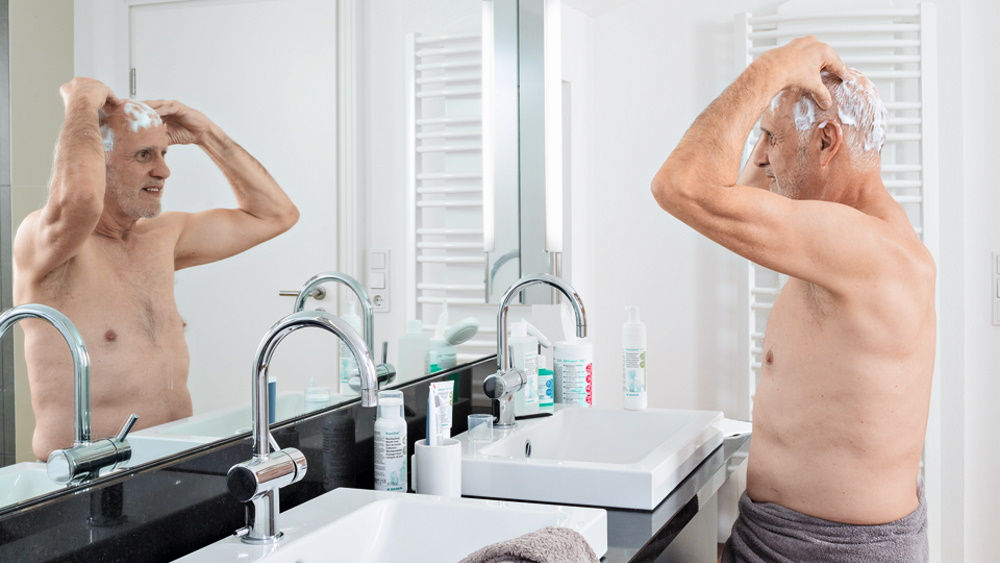 Homme âgé devant un miroir dans une salle de bain privée effectuant une décolonisation de l’ouïe et de la tête