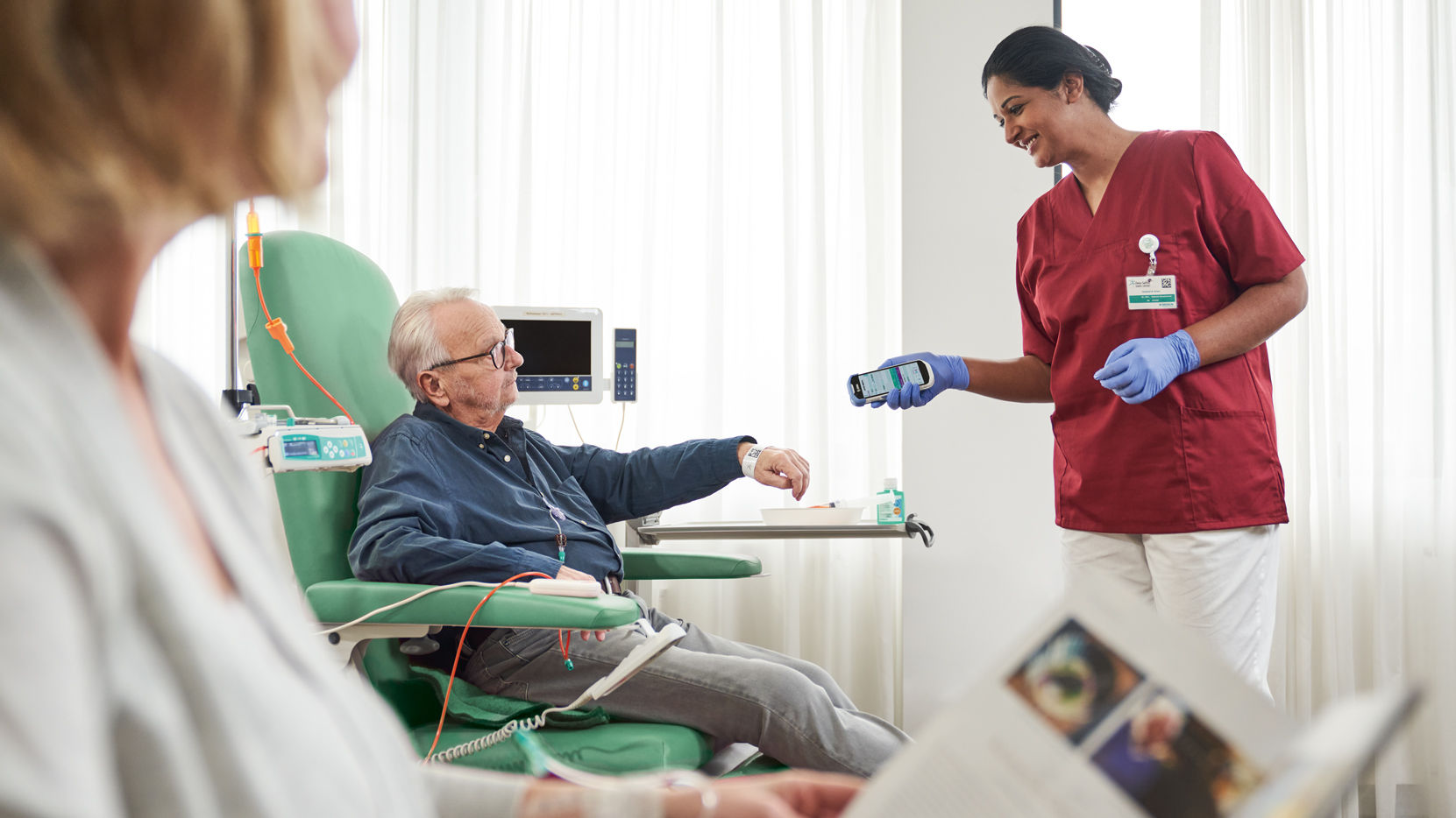 oncology-patient-with-glasses-sitting-on-the-chair-and-nurse-with-gloves-scanning-patient-identification-on-wristband-for-safety-and-documentation-in-dayclinic