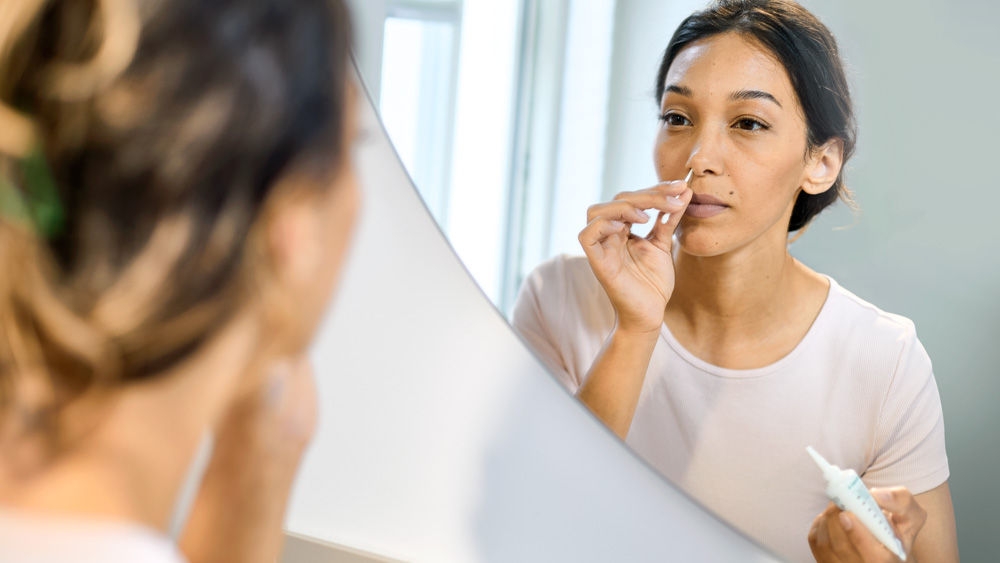 femme effectuant un rinçage nasal antimicrobien à la maison devant le miroir de bain