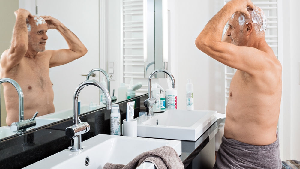 Homme âgé devant un miroir dans une salle de bain privée effectuant une décolonisation de l’ouïe et de la tête.