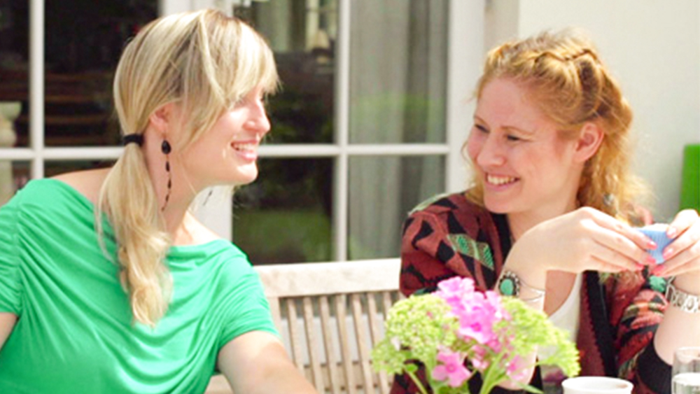 Une femme souriant et discutant avec son amie dans un jardin portant un dispositif médical pour soulager ses symptômes d’hydrocéphalie.