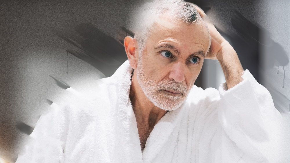 Un patient âgé dans un peignoir se regarde dans le miroir de la salle de bains.