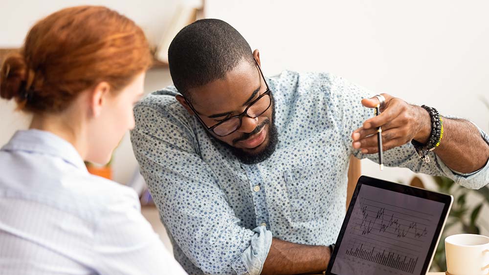 Deux personnes discutant de graphiques d’entreprise et de diagrammes sur une tablette dans un bureau. 